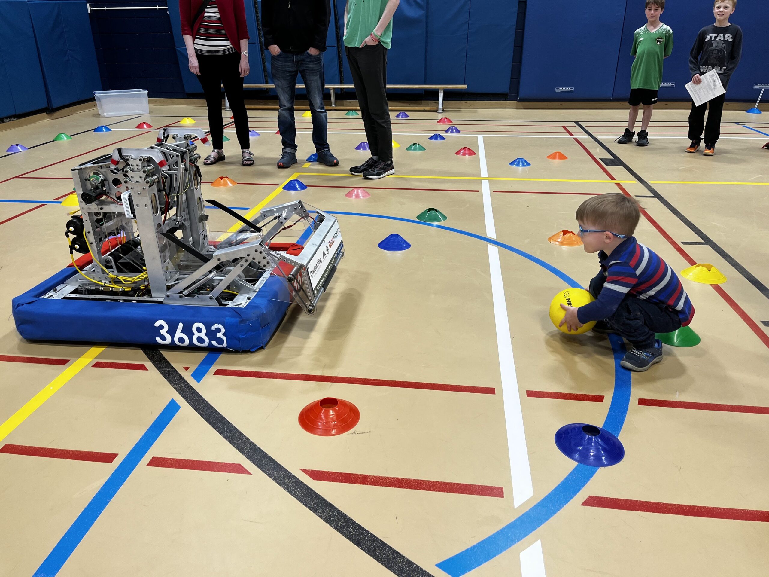 A child holds a ball ready to roll it toward a robot